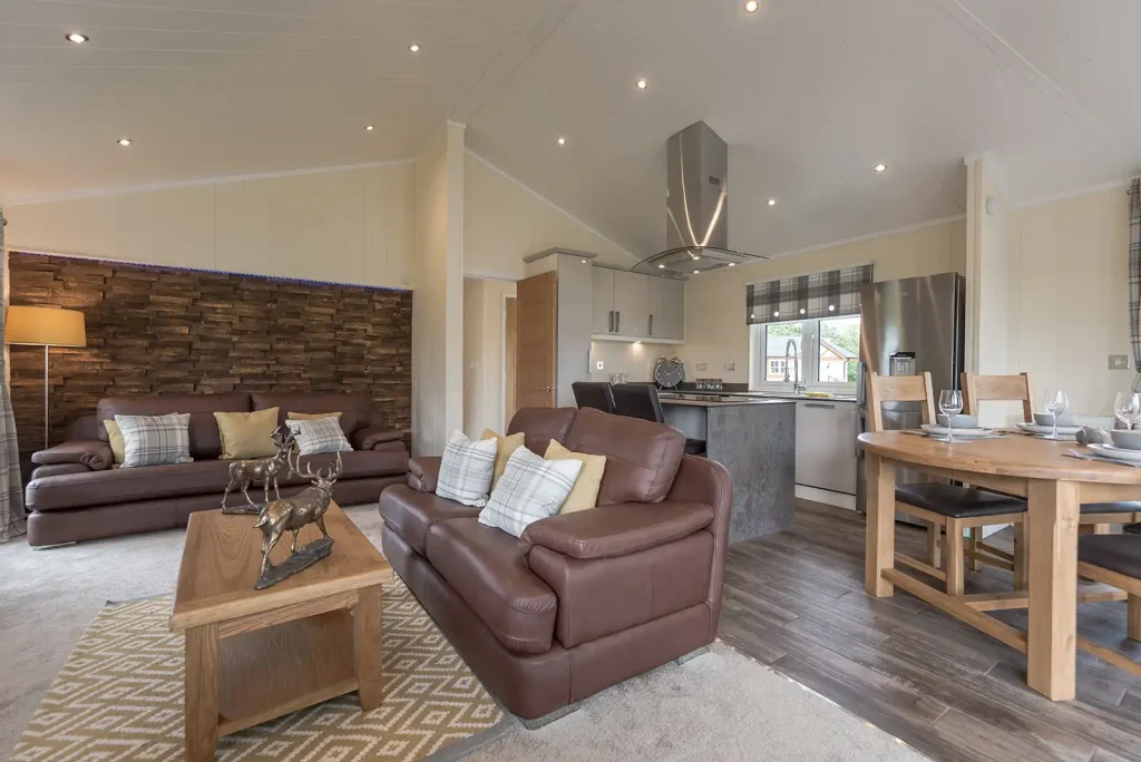 Harvard Lodge sitting area with leather sofas, feature wall, and open-plan kitchen at Paradise Lakeside Lodges.