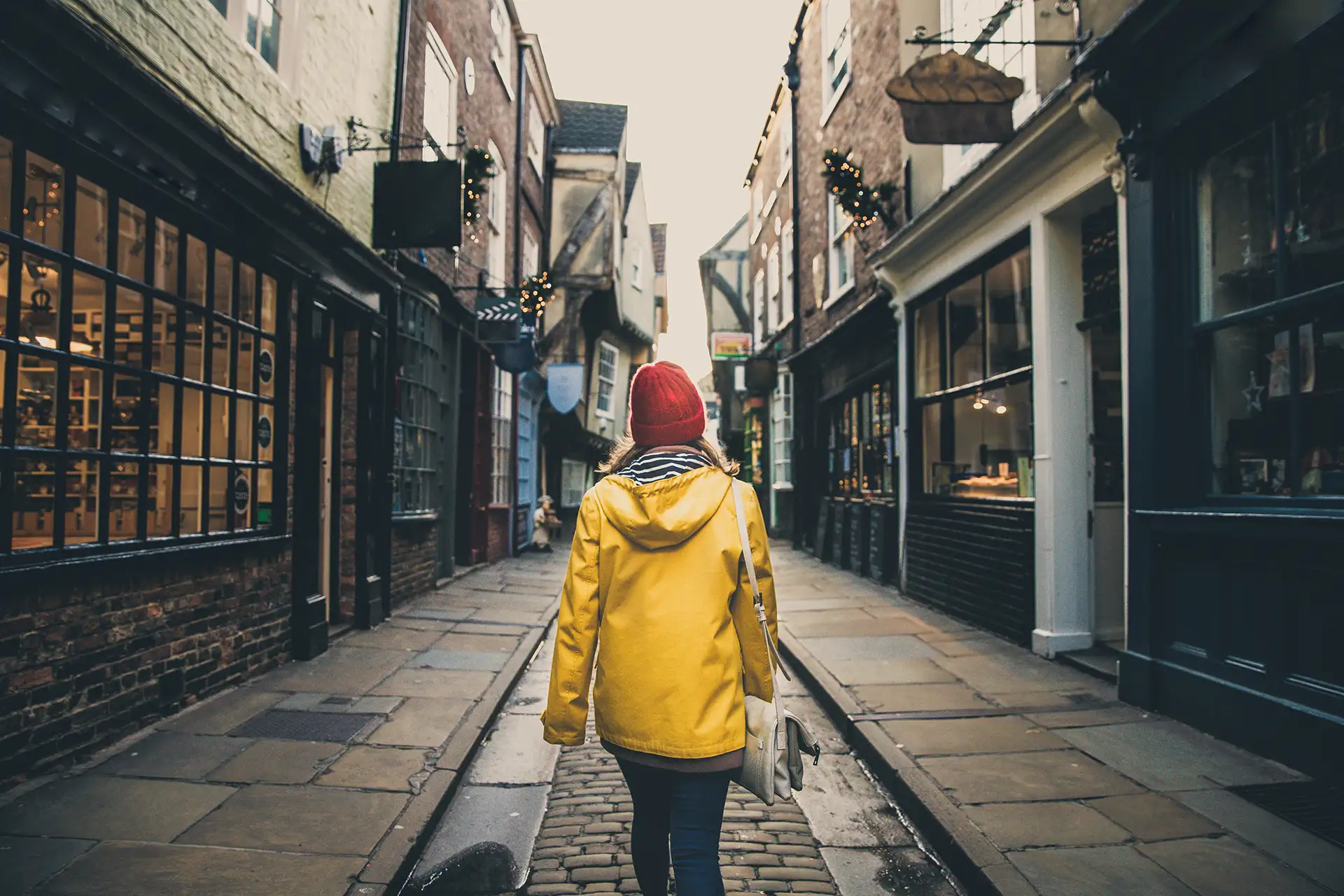 Woman in yellow coat walking through The Shambles in York.